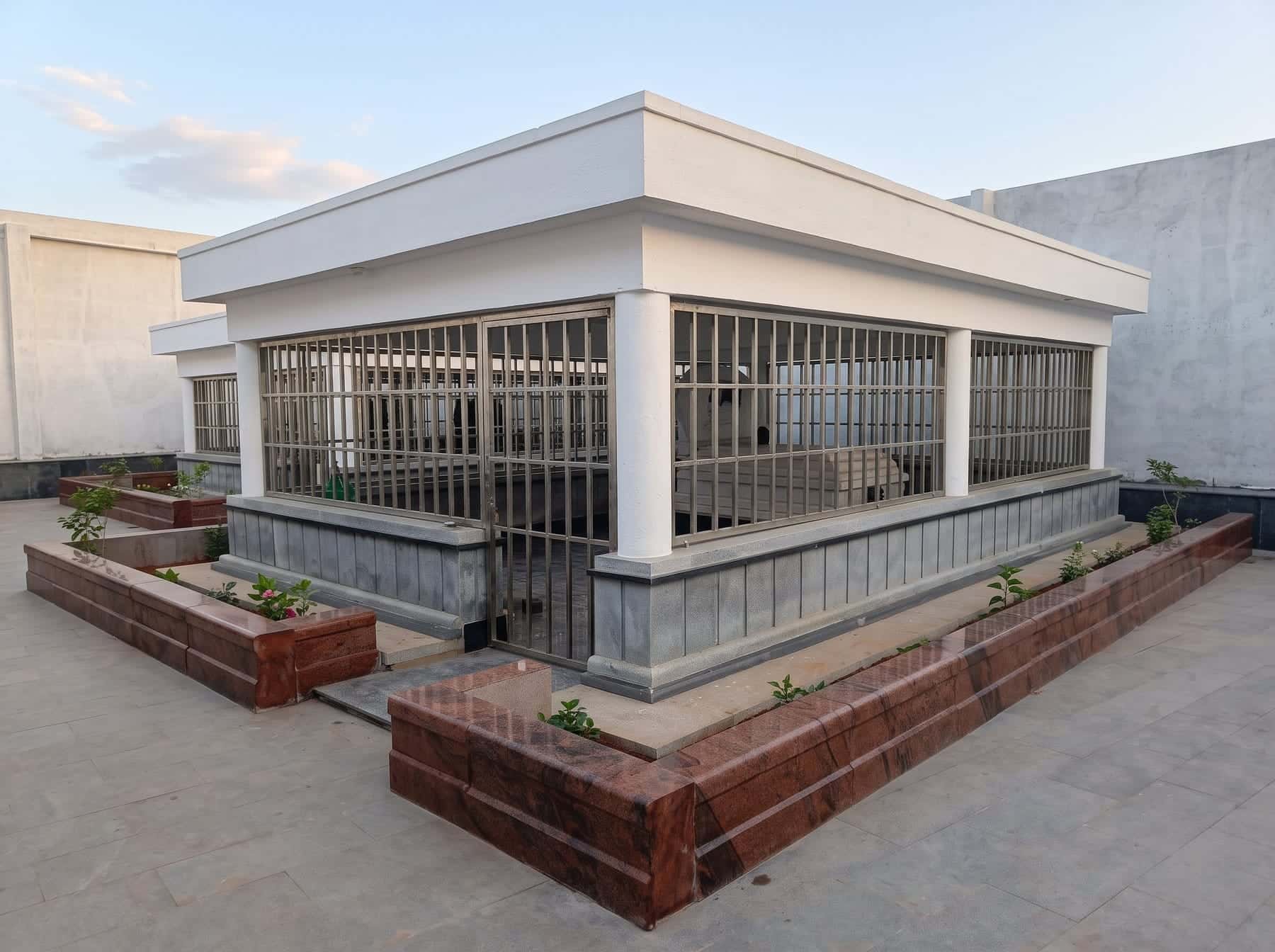 Enclosed granite samadhi structure with grille walls and red granite planters
